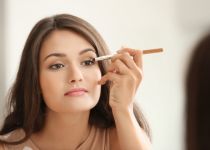 Beautiful girl applying cosmetics in front of mirror